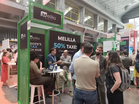 Stand de iMelilla Digital Hub en South Summit, con estructura metálica verde y visitantes reunidos en torno a las mesas.